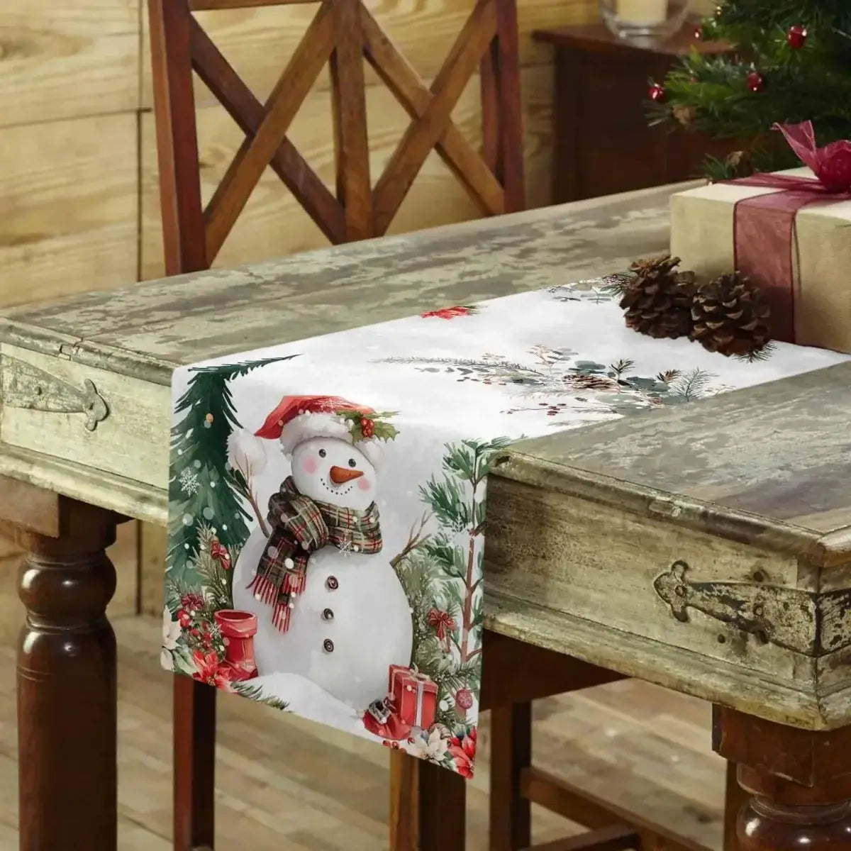 Christmas-themed linen table runner featuring a snowman and gift boxes on rustic wooden table. Ideal for holiday gatherings and festive decor.