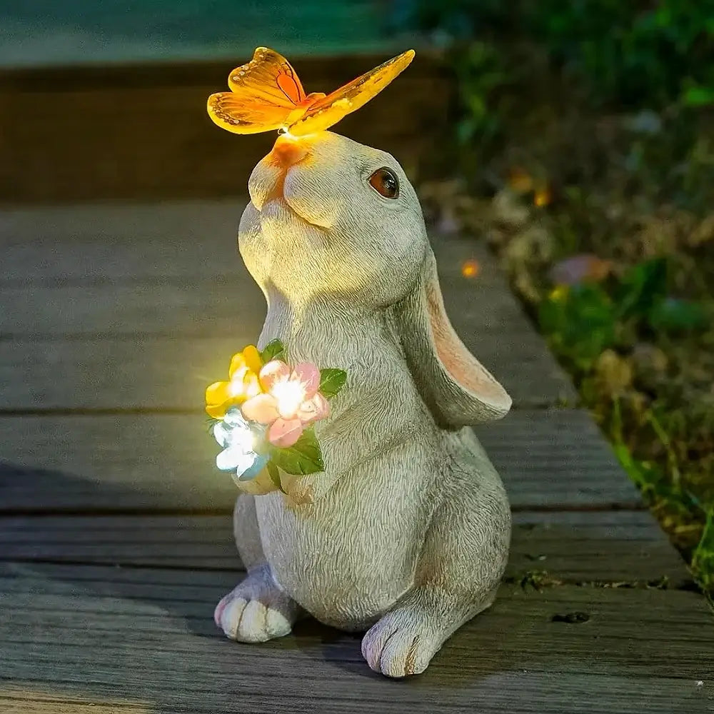 Solar Bunny Statue Decor with glowing LED butterfly and flower lights, ideal for garden paths or patios. Weather-proof and UV-resistant resin design.