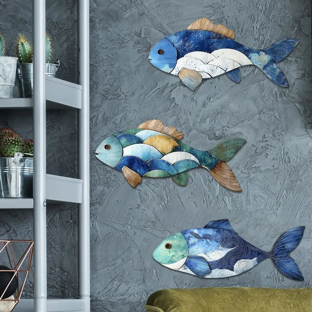Set of three wooden fish wall figurines in blue and brown tones on a gray interior wall. Perfect for coastal-themed home decor.
