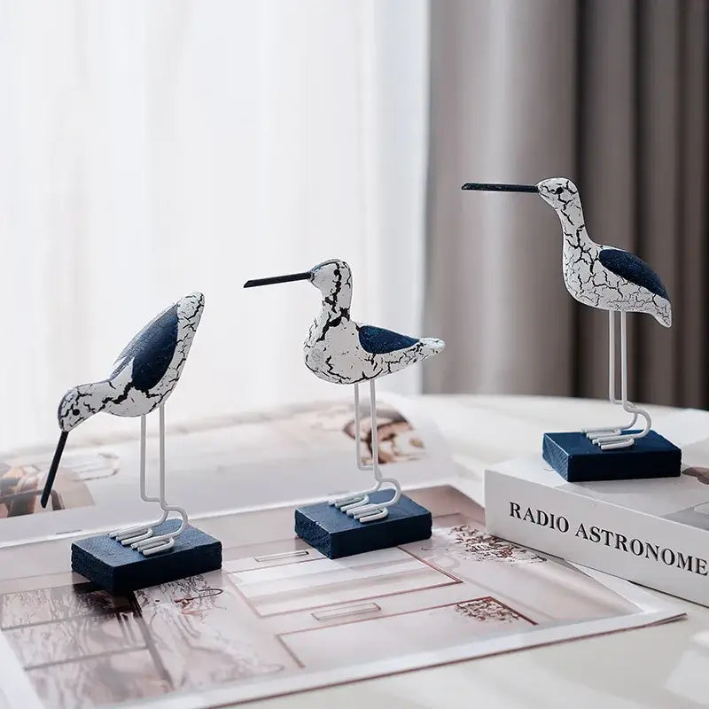 Coastal-style 3pcs wooden seagull figurines featuring white crackled texture and navy accents, displayed on a modern table setup.