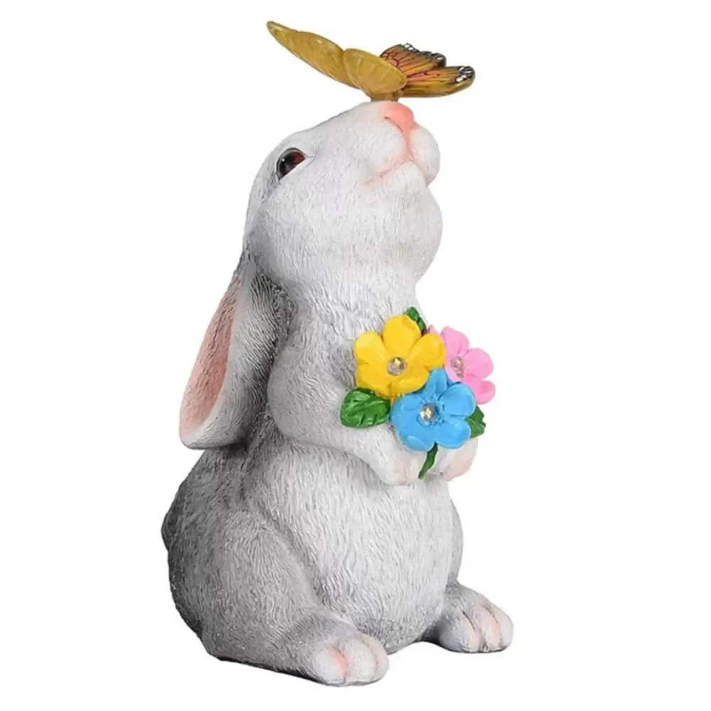 Close-up of Solar Bunny Statue holding colorful LED flowers with butterfly on nose. Resin garden sculpture for outdoor decoration.