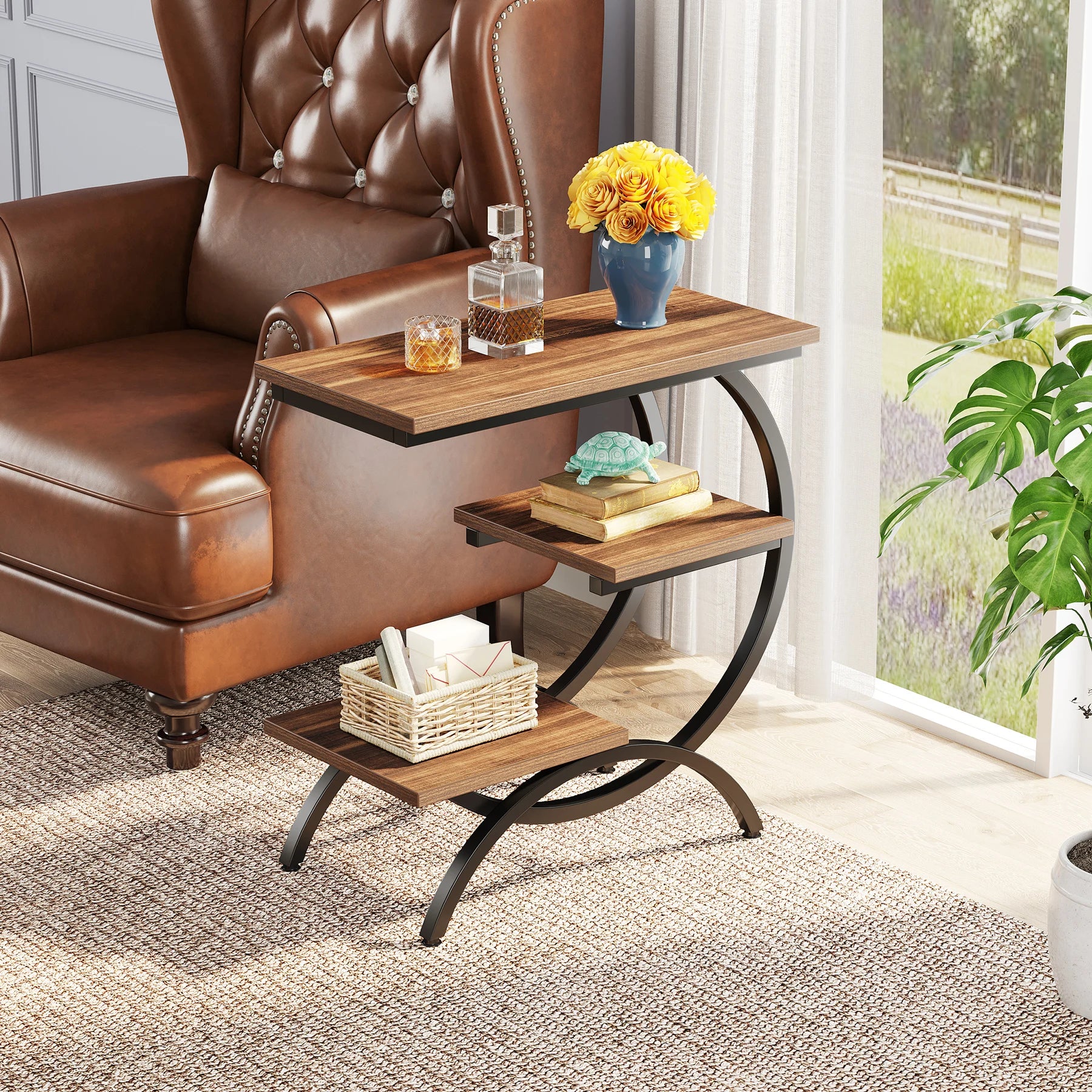 Industrial C-shape 3-tier end table with wood finish, placed next to a leather armchair with flowers and books on display.
