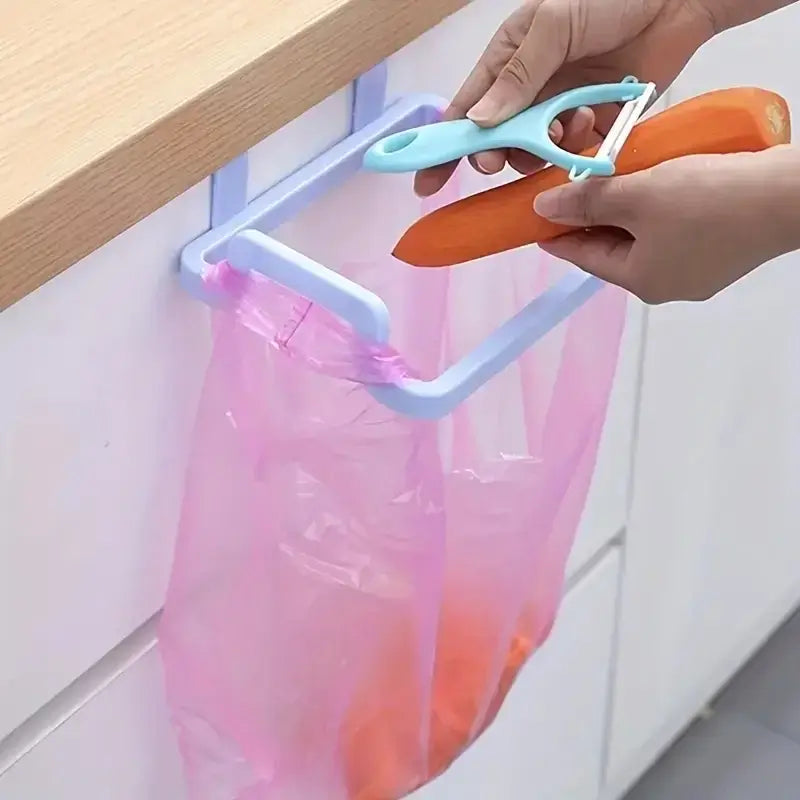 Blue under sink trash bag hook holding a pink bag while peeling vegetables. Easy kitchen waste disposal with no-drill cabinet mount.