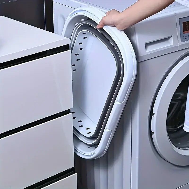 Collapsible laundry basket stored compactly between washer and cabinet, ideal for space-saving laundry organization.