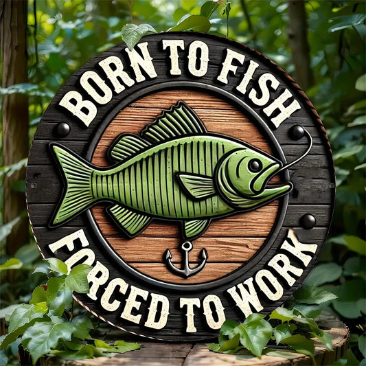 Fishing Enthusiast metal sign with green fish and 'Born to Fish, Forced to Work' text, displayed outdoors among green foliage.