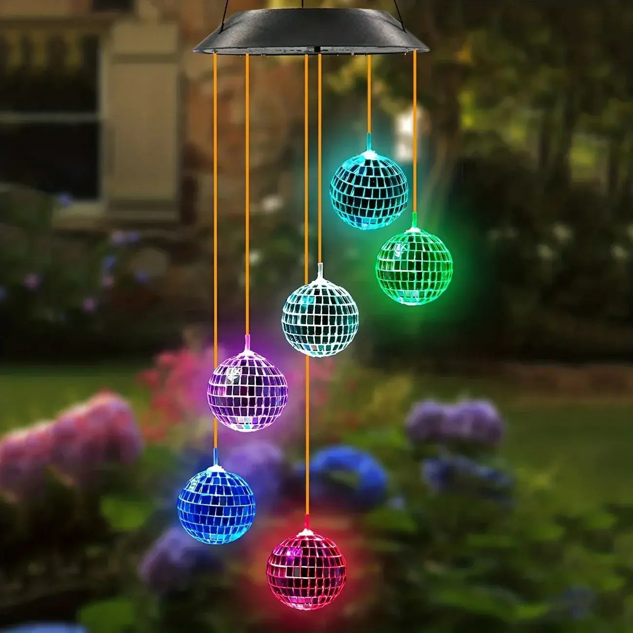 Hanging LED Morocco Ball Solar Wind Chime Light in a garden setting, glowing in vibrant colors among flowers and greenery.