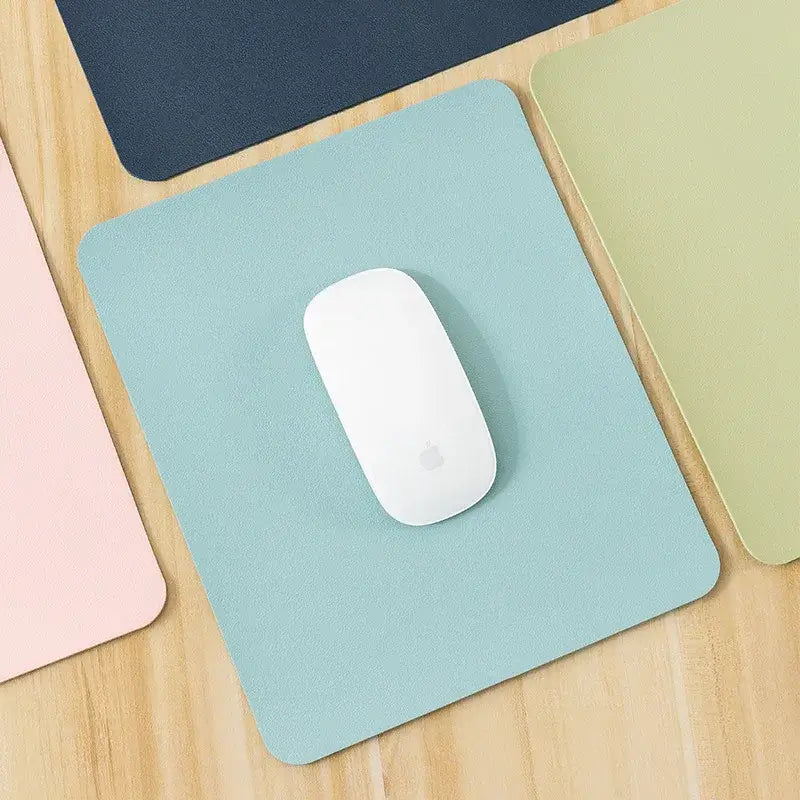 Sky blue Small PU Leather Gaming Mouse Pad with non-slip base, shown on a wooden desk with a white mouse.