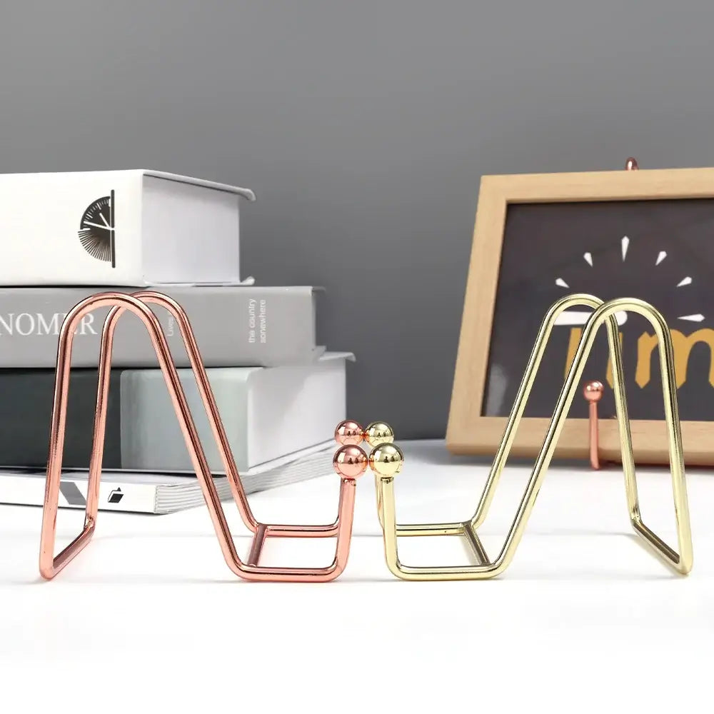 Gold and rose gold art display frame stands on a desk. Stylish holders for photo frames or books in home decor.